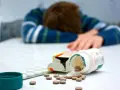 Osoba w bluzie leży na stole, obok rozsypane tabletki, w tym opakowanie leku Seronil 10 mg.