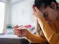 Kobieta z opuszczoną głową trzyma test ciążowy. Jej dłoń z czerwonym lakierem do paznokci zaciska się na teście. Tokofobia może wywoływać takie emocje.