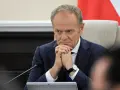 Mężczyzna w garniturze, z zaciętą miną, wygląda jak pesymista. Dłonie splecione, wzrok utkwiony w dal.