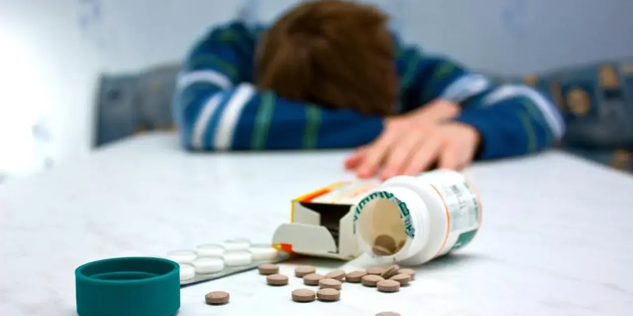 Osoba w bluzie leży na stole, obok rozsypane tabletki, w tym opakowanie leku Seronil 10 mg.
