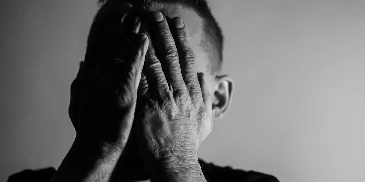 Mężczyzna zakrywa twarz dłońmi, symbolizując wyczerpanie i walkę z neurastenią.