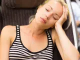 Blondynka z opartą o dłoń głową, oczy zamknięte, widać głębokie zmęczenie po długiej podróży.