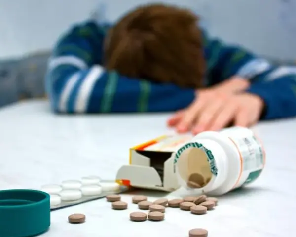 Osoba w bluzie leży na stole, obok rozsypane tabletki, w tym opakowanie leku Seronil 10 mg.