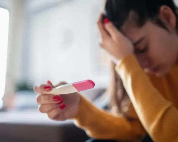 Kobieta z opuszczoną głową trzyma test ciążowy. Jej dłoń z czerwonym lakierem do paznokci zaciska się na teście. Tokofobia może wywoływać takie emocje.