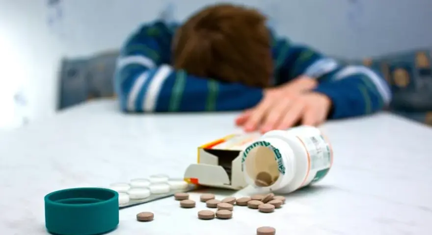 Osoba w bluzie leży na stole, obok rozsypane tabletki, w tym opakowanie leku Seronil 10 mg.