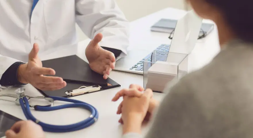 Lekarz omawia z pacjentem diagnozę, być może f43 kod choroby. Na stole stetoskop i laptop.