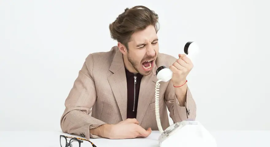 Mężczyzna w garniturze krzyczy do telefonu, jego twarz wyraża złość. Widać, że jest cholerykiem.