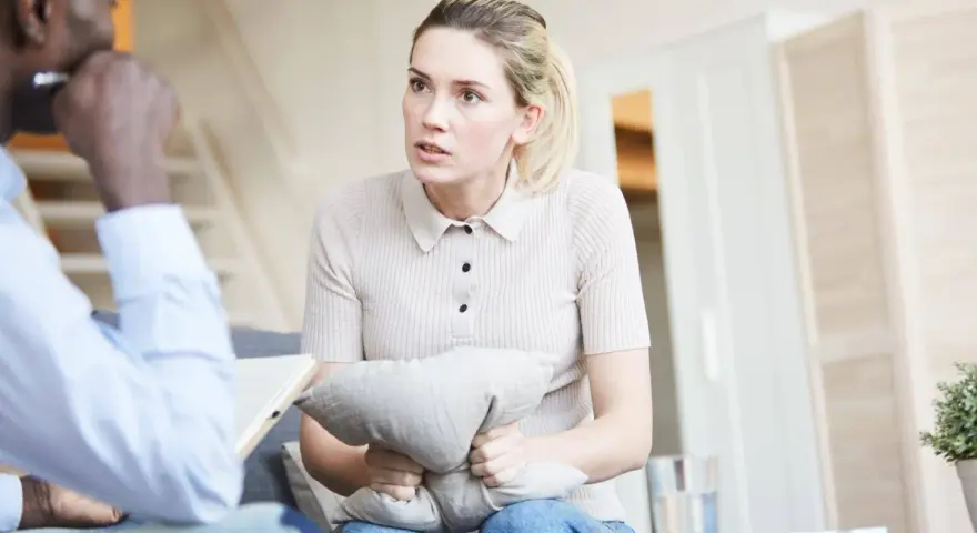 Kobieta w trakcie sesji u psychiatry, ściska poduszkę, szukając ukojenia.