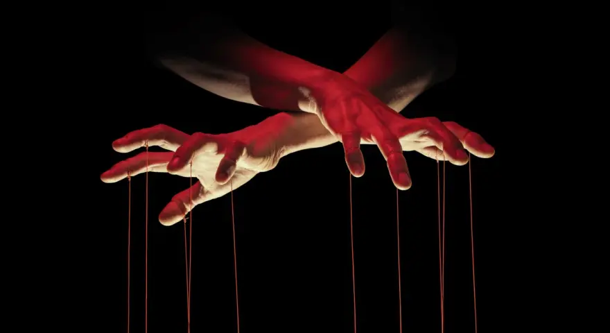Dłonie jak marionetka, sterujące sznurkami. Czerwone światło podkreśla makiawelizm i manipulację.