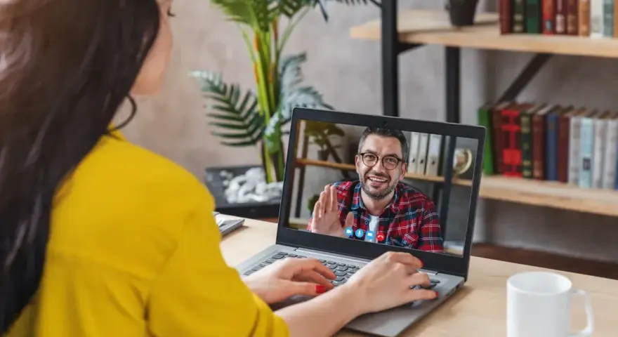 Kobieta na wideo rozmowie z mężczyzną, który uśmiecha się i macha. Może to być konsultacja online, np. test na autyzm.