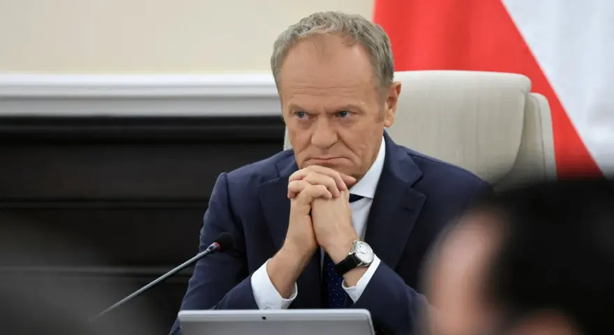 Mężczyzna w garniturze, z zaciętą miną, wygląda jak pesymista. Dłonie splecione, wzrok utkwiony w dal.