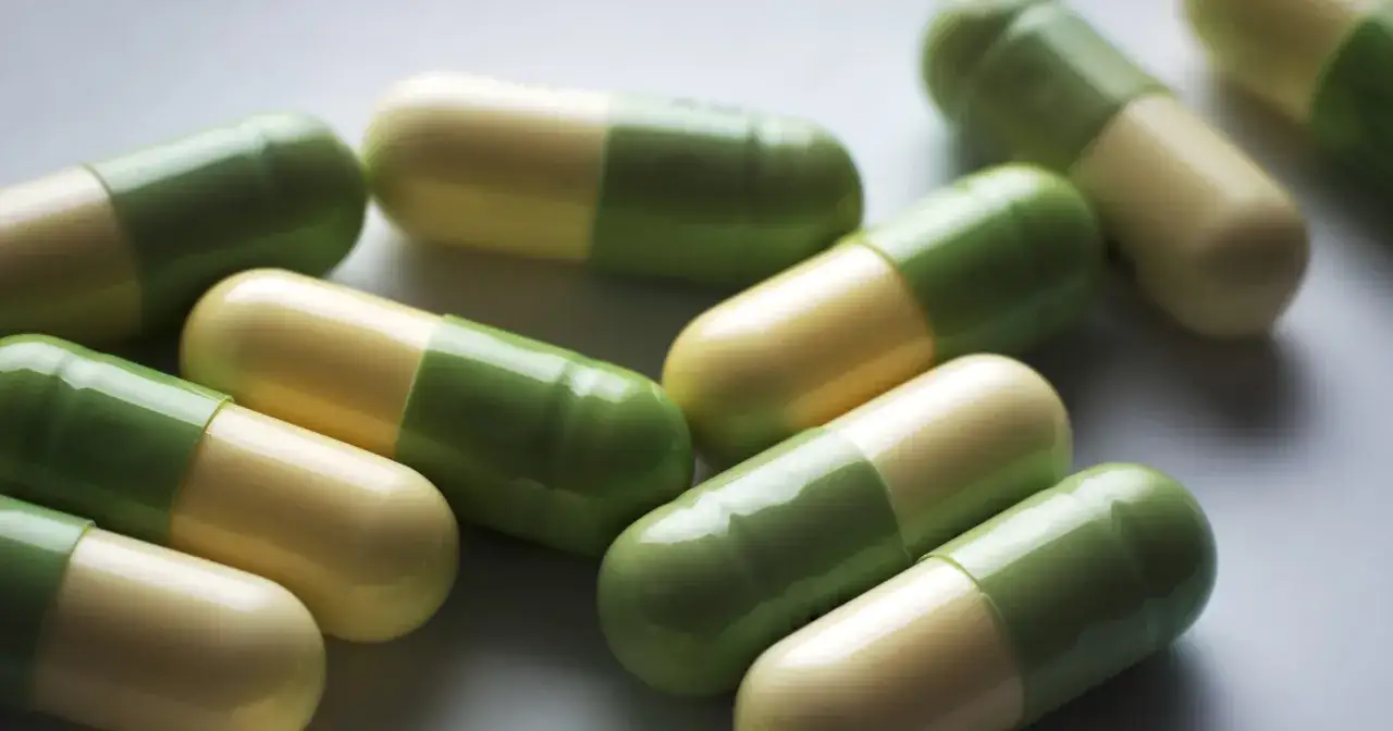 Kapsułki leku Seronil 10 mg, dwukolorowe, zielono-żółte, leżą na jasnym tle.