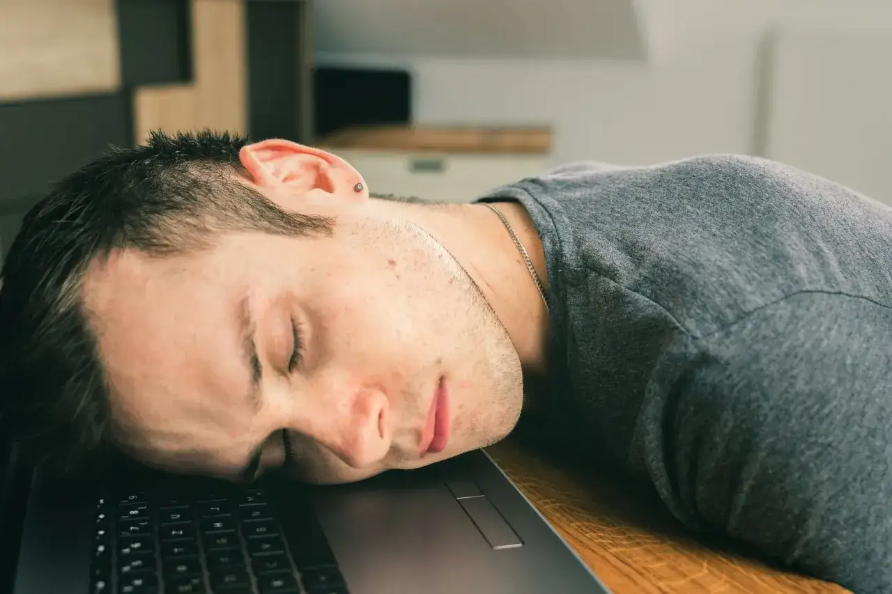 Mężczyzna śpi na klawiaturze laptopa, pogrążony w marazmie.